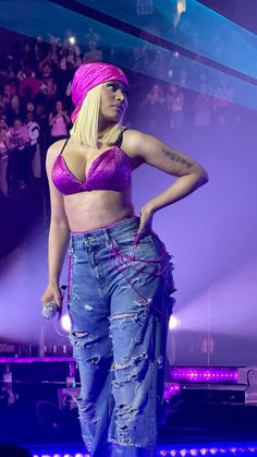 a woman in a pink bra top and jeans on stage with her hands on her hips