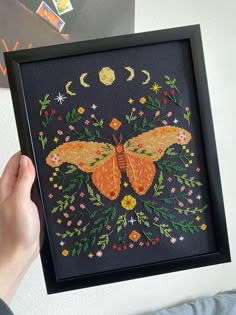 a person holding up a cross - stitch picture with a butterfly on it's wings