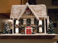 a gingerbread house decorated for christmas with lights and snow on the roof, trees and bushes