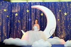 a woman in a white dress is sitting on the moon with clouds and stars around her