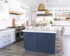 a large kitchen with white cabinets and blue island counter tops, gold pendant lights over the sink