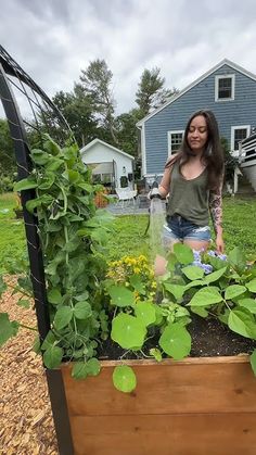 a woman standing next to a wooden planter filled with plants