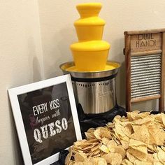 a table topped with chips next to a bowl of guacamole and a sign that says every kiss begins with queso