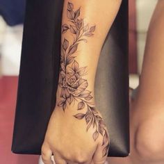 a woman's hand with a flower tattoo on her arm and wrist, holding a black bag