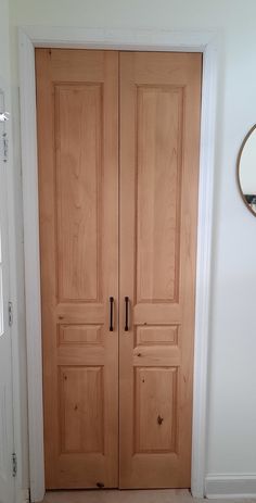 an empty room with two wooden doors and a round mirror on the wall above it