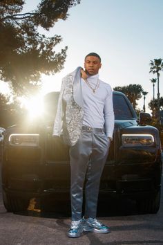 a man standing in front of a black truck with his hand on his hip while wearing silver shoes