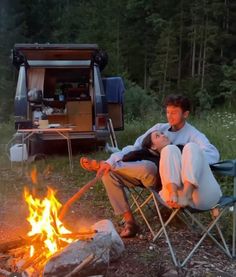 two people sitting in chairs around a campfire