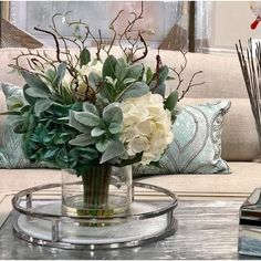 a vase with flowers sitting on top of a glass table next to a couch and pillows