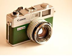 an old fashioned camera sitting on top of a white table next to a brown and green lens