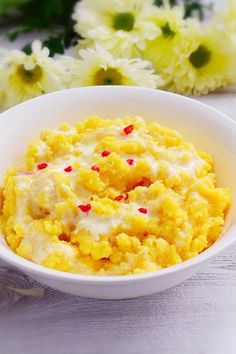 a white bowl filled with mashed potatoes on top of a table next to flowers