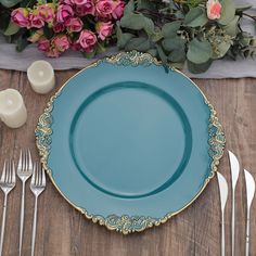 a blue plate sitting on top of a wooden table next to silverware and flowers