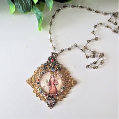 "A glass cabochon encases a Vintage picture of Mother Mary holding Jesus and flowers. This unique piece has been  embellished with an array of shimmering rhinestones, decorative brass filigrees and dangles from a 28\" (inch) Czech crystal rosary chain with a lobster claw closure. Measures: 1.5\" x 1.5\" Chain ~ 28 inch Thank You for visiting my Shoppe.... Have a peek at all my other listings: www.etsy.com/CharmainesWhimzy Merci Beaucoup Please note: This is individually crafted work of  art, any irregularities are intentional  and do not diminish the quality of the piece in any way." Mother Mary Rosary, Picture Of Mother, Mary Holding Jesus, Mother Mary Pictures, Crystal Rosary, Vintage Picture, Holy Mary, Mary And Jesus, Rosary Chain