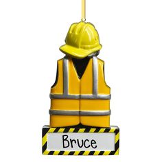 a yellow construction worker ornament hanging from a hook on a white background with the word bruce written in black