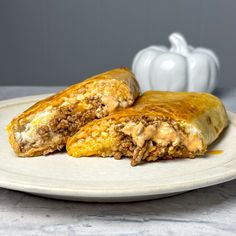 two burritos on a white plate next to a pumpkin