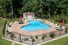 an aerial view of a backyard with a pool and fenced in area, surrounded by trees