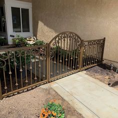 an iron gate in front of a house with flowers growing on the ground next to it