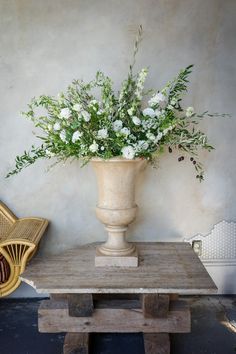 a vase with white flowers sitting on top of a wooden table next to a wicker chair