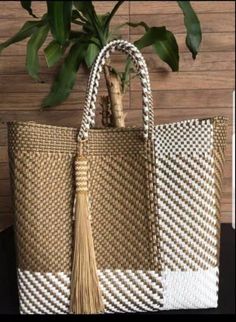 a white and beige bag with a tassel hanging from it's side next to a potted plant