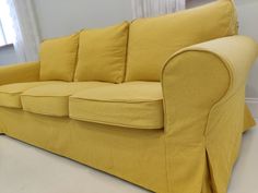 a yellow couch sitting in front of a window next to a white wall with curtains