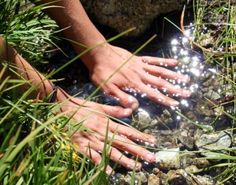 someone is washing their hands in a stream of water with rocks and grass around them