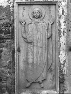 a black and white photo of a statue on the side of a building with an image of jesus holding his hands up