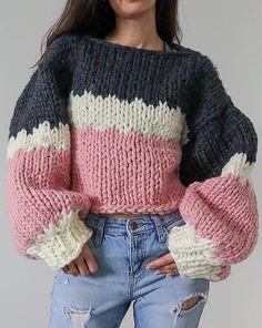 a woman wearing ripped jeans and a pink, black, white and grey sweater with puffy sleeves