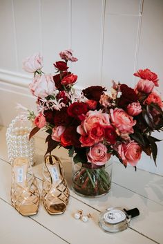 a vase filled with red and pink flowers next to two pairs of high heeled shoes