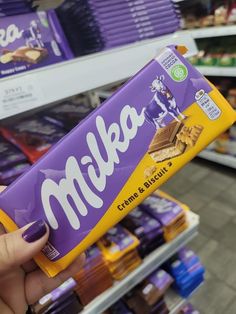 a person holding up a bar of milk chocolate in a grocery store aisle with other items on the shelves