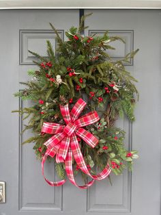 a christmas wreath on the front door with red berries and greenery tied around it