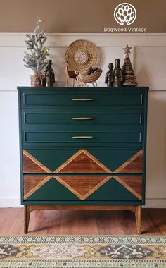 a green dresser with wooden drawers and decorative items on top, in front of a white wall