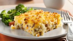 a white plate topped with lasagna and broccoli next to a fork