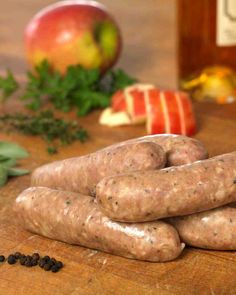 several sausages on a wooden cutting board next to an apple and pepper shaker