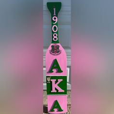 a pink and green wooden sign with the word ak on it