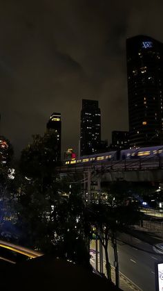 the city skyline is lit up at night with skyscrapers in the foreground and cars on the road below