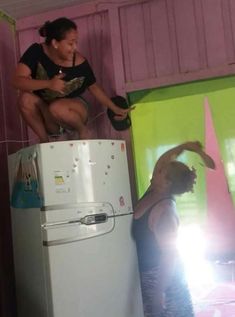 two women sitting on top of a refrigerator in a pink and green room next to each other