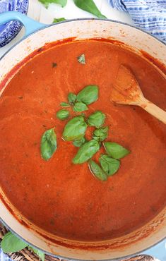 a bowl of tomato soup with basil leaves on top and a wooden spoon in it