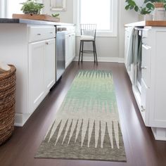 a kitchen area with white cabinets and wooden floors, along with a rug on the floor