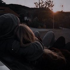 two people sitting in the back of a car watching the sun go down behind them