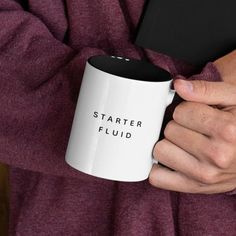 a person holding a coffee mug with the words starter fluid printed on it's side