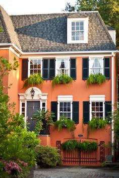 an orange house with black shutters and green plants growing on the side of it