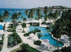 an outdoor swimming pool surrounded by palm trees and blue water with boats in the background