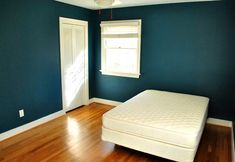 an empty bedroom with blue walls and wood flooring is pictured in this image, there is a mattress on the bed