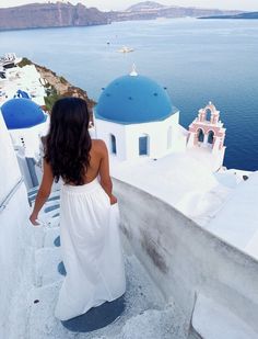 a woman in a white dress is walking up the stairs to a blue domed building