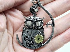 The Steampunk Owl Sitting on a Tree Branch Necklace is a captivating piece that marries the wisdom of nature with the intricate mechanics of steampunk design. The pendant features a detailed owl perched on a tree branch, its body adorned with gears and cogs that evoke a sense of retro-futuristic charm. The combination of organic and mechanical elements creates a striking visual contrast, making this necklace a standout accessory. Suspended on a 22-inch stainless steel chain, the pendant's cool m Steampunk Style Chain Jewelry As Gift, Fantasy Metal Necklaces For Collectors, Steampunk Silver Necklace With Round Pendant, Silver Steampunk Necklace With Round Pendant, Steampunk Silver Metal Necklaces, Steampunk Silver Pendant Necklace, Steampunk Silver Round Pendant Jewelry, Silver Steampunk Metal Necklace, Silver Steampunk Pendant Necklace