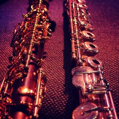 two saxophones sitting side by side on top of a purple surface with other musical instruments in the background