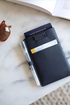 a passport, pen and sunglasses on a marble table next to an open notebook with a yellow stripe