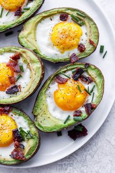 four avocado halves with eggs and bacon on them sitting on a white plate