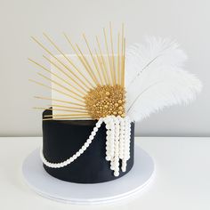 a black and white cake with gold decorations on it's top, decorated with feathers