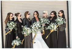 a group of women standing next to each other in front of a wall holding bouquets