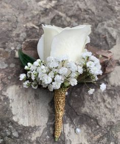 a white rose and baby's breath boutonniere sitting on a rock